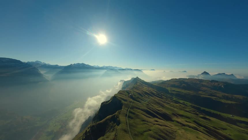 A mountain range with rugged peaks rises under the sunny sky its atmosphere softened by drifting fog