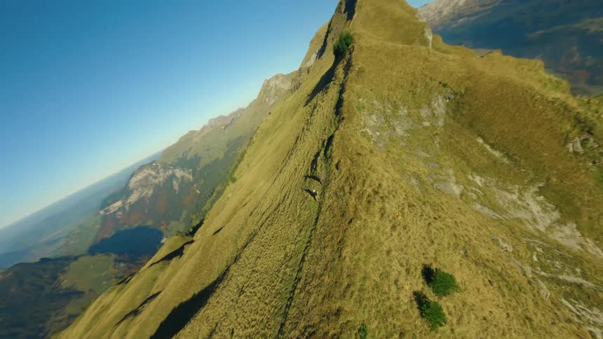 Two hikers walk along a ridge in the Swiss mountains overlooking an ocean of clouds on a sunny day