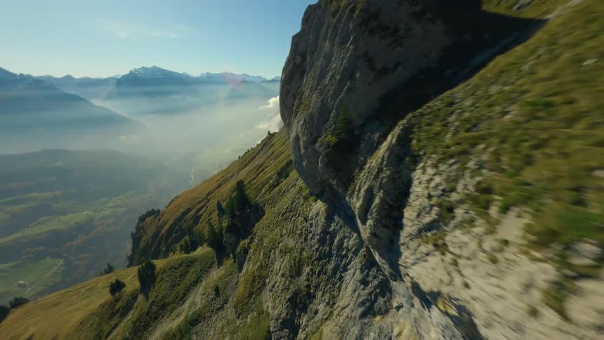 Aerial of grassy mountainside above a wide valley under bright sky