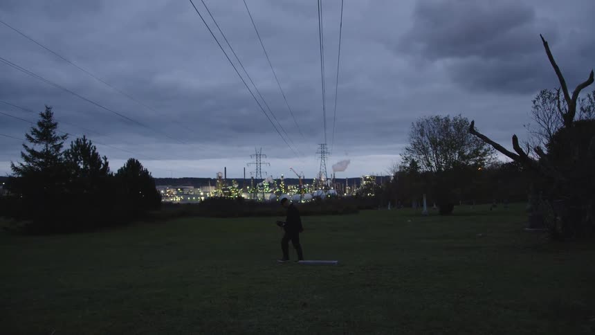 A man walks across a grassland beneath power lines at dawn with a distant power plant visible on the horizon