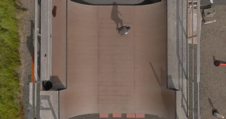 A skateboarder practicing tricks on a wooden half pipe ramp in a skate park with their elongated shadow dancing across the surface