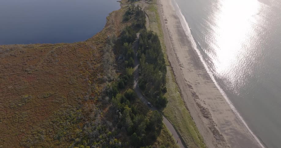 A coastal road stretches forward on a sunny day with a lake on each side