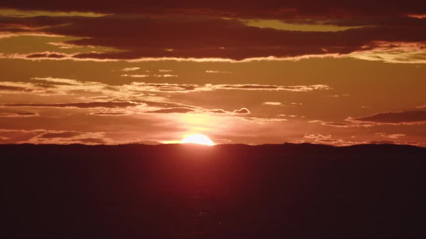 Sun setting on the horizon beneath orange clouds
