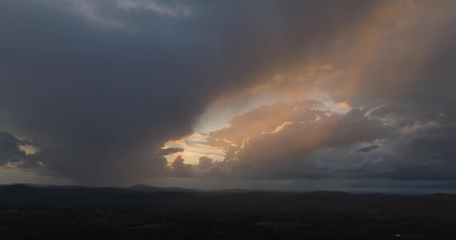 Dramatic sky with dark clouds and golden light over silhouette of mountainous terrain