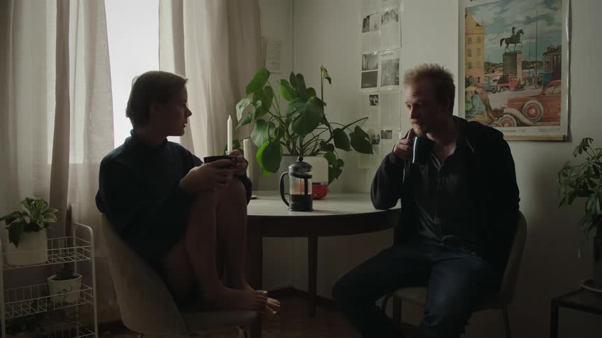 Two people sitting in a kitchen lit by natural light drinking coffee