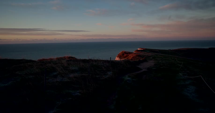 The sun sets over a large expanse of ocean illuminating the edge of the water and the far coastal cliffs