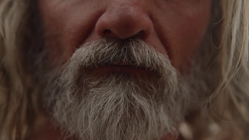 A very closeup shot focuses on the lower face of a person with long hair showing the texture and volume of their long full gray beard and mustache