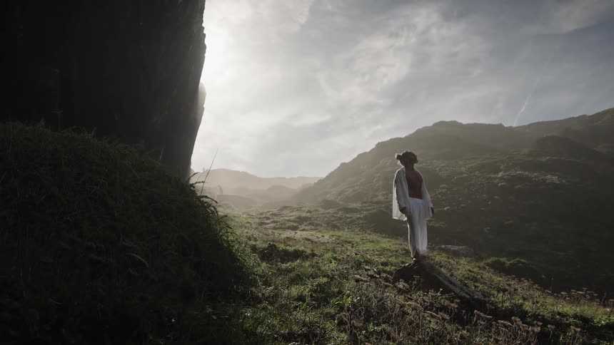Person standing on a rock in a mountainous landscape lit by the sun through clouds