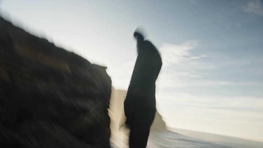 Man moving expressively on rocky terrain near the ocean