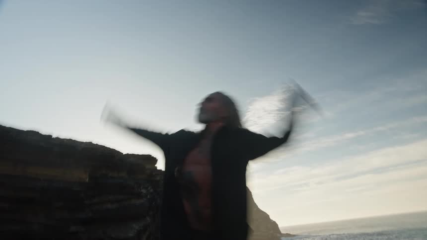 Man with arms outstretched in motion by the seaside at sunset