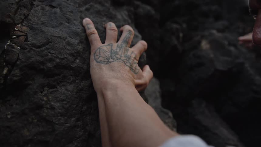 Tattooed hand with white sleeve touching dark rock with rough texture