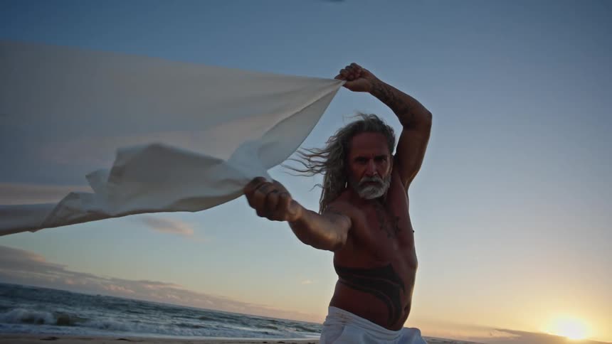 The man waves around a white sheet on the beach