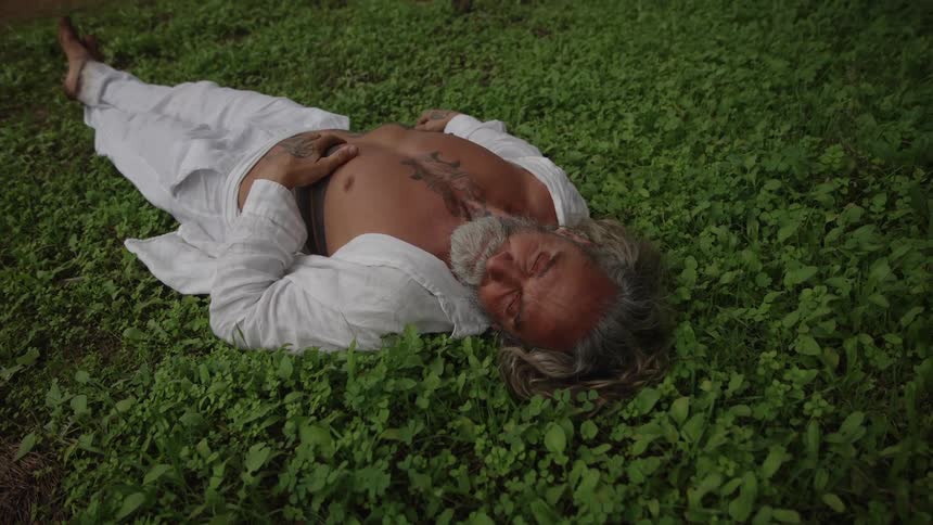 Graybearded man rests on the grass with a serene expression