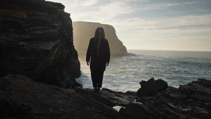 The waves hit the rocks where the man is standing
