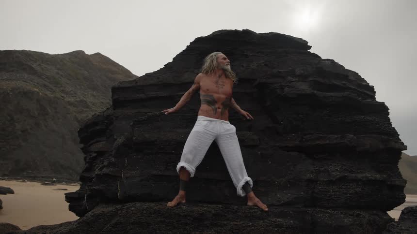 The man is standing on a large boulder on the shore