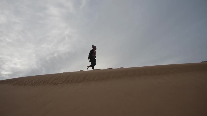 Man walks along the top of a dune on an overcast day