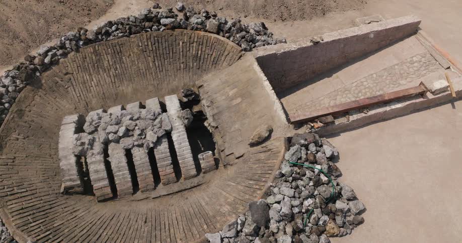 Circular structure with rectangular blocks arranged in a regular pattern surrounded by rocks and access ramp