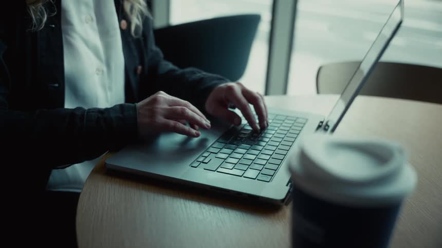 A person typing on laptop with coffee on wooden table