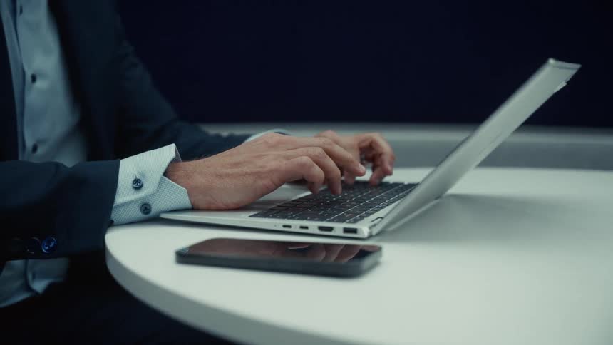 Closeup of a person in a suit working on a laptop in a room
