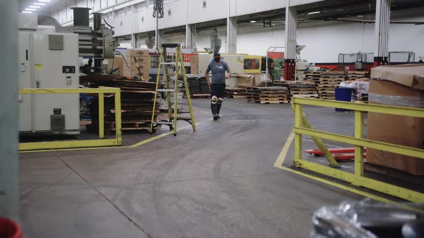 Workers move materials inside a large industrial warehouse under bright lighting