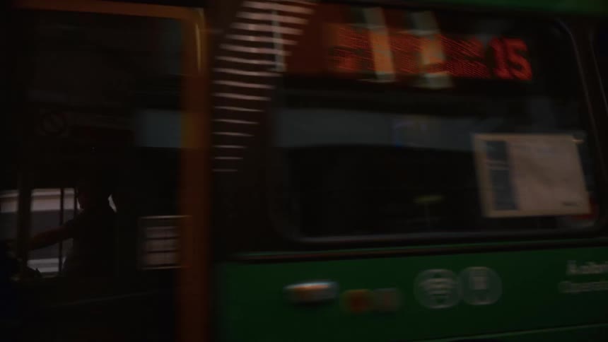 The front and side of a moving doubledecker bus painted green and yellow are shown in closeup as the vehicle drives quickly along an urban street