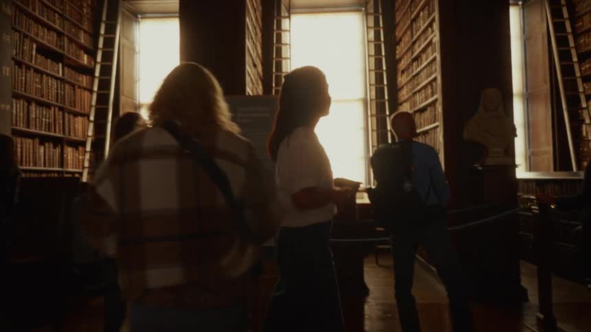 A woman is walking through a library and there are many men and women are present already