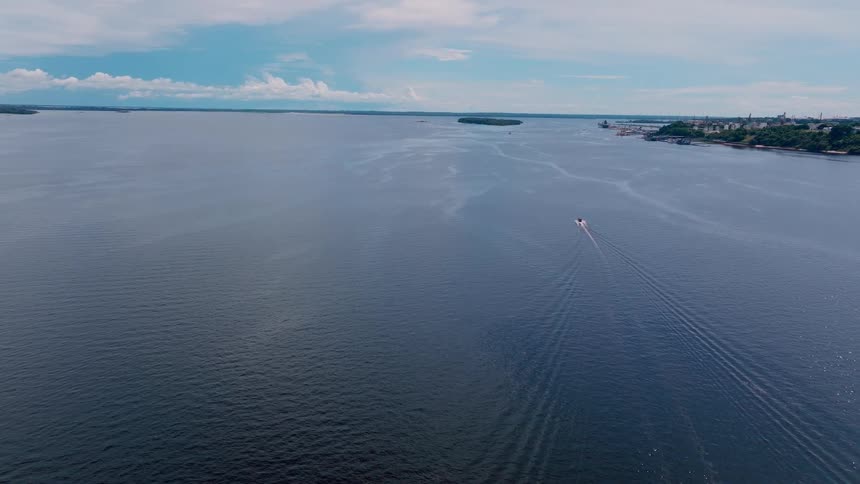 Aerial shot of a speedboat leaving a wake on blue water under a cloudy sky