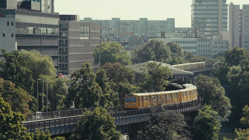Two overhead trains move in opposite directions through the city their tracks surrounded by trees
