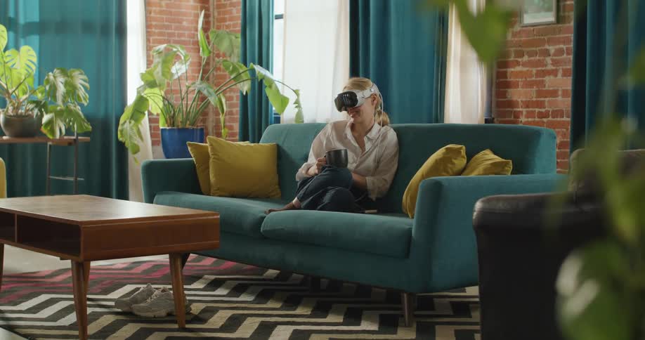 Woman with vr headset holding a mug on a sofa in a living room