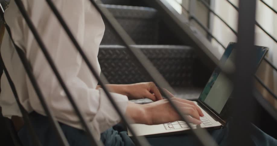 Close up of a young woman using a laptop computer while sitting on a staircase indoors during daytime