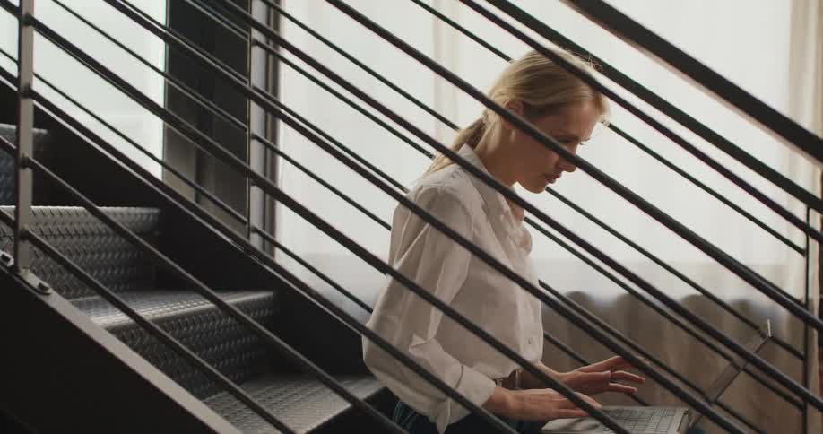 Woman sits on a metal staircase working on a laptop