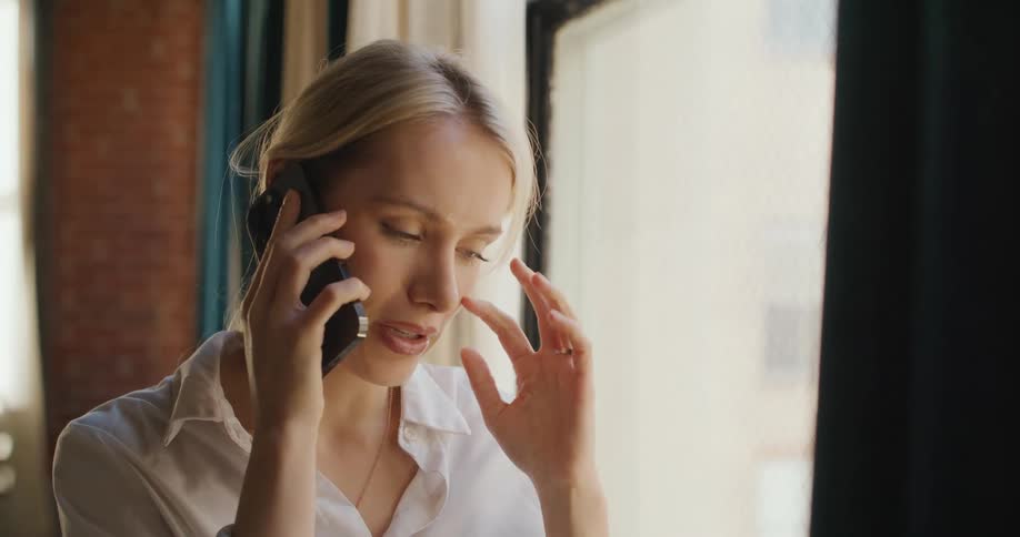 A young blonde woman holding a phone to her ear talking to someone