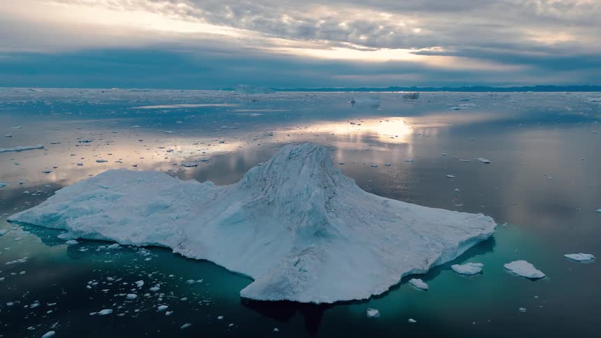 Aerial view of flat iceberg with peak floating in dark water under evening sky