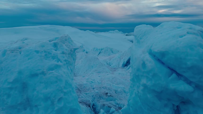 An aerial view showcases a vast expanse of icy blue glacial terrain under an overcast sky