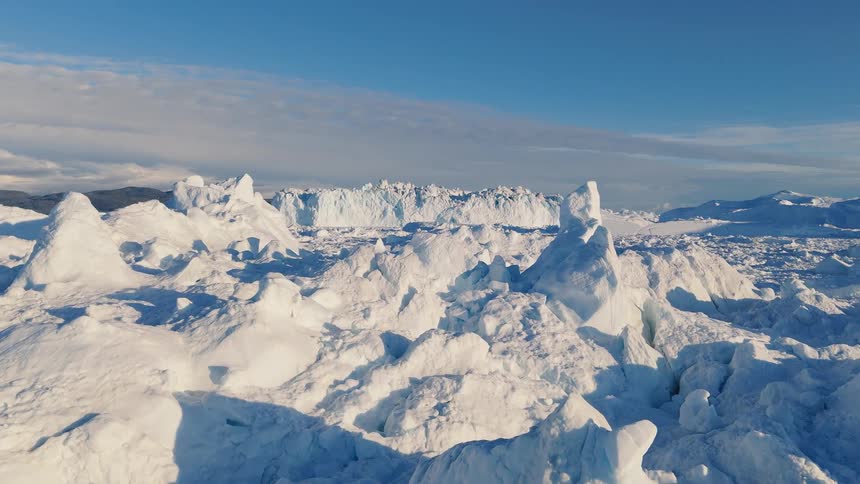 A sunlit expanse of rough sea ice and jagged ridges stretches toward distant dark hills beneath a clear blue sky