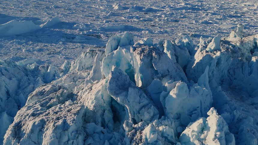 The video is a sweeping aerial shot of a massive jagged glacier composed of white and pale blue ice the terrain is incredibly uneven with towering sculpted peaks and deep fissures suggesting the powerful movement and breakup of the glacial ice m