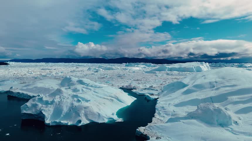 A sunlit panorama of rough sea ice and ridges stretches toward distant low hills beneath a clear sky
