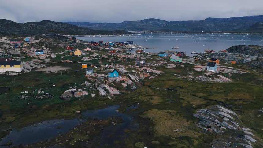 Small houses are spread across a barren mosscovered landscape dark hills and a body of water rise behind the settlement under a gray sky