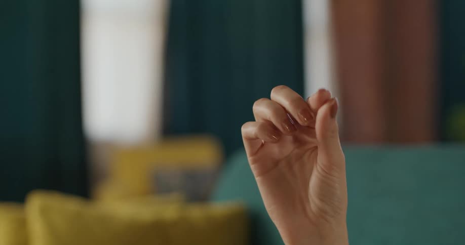 A womans hand quickly makes a pinching gesture with two fingers against a softly blurred background