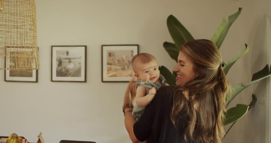 A smiling mother embraces her baby in a bright room