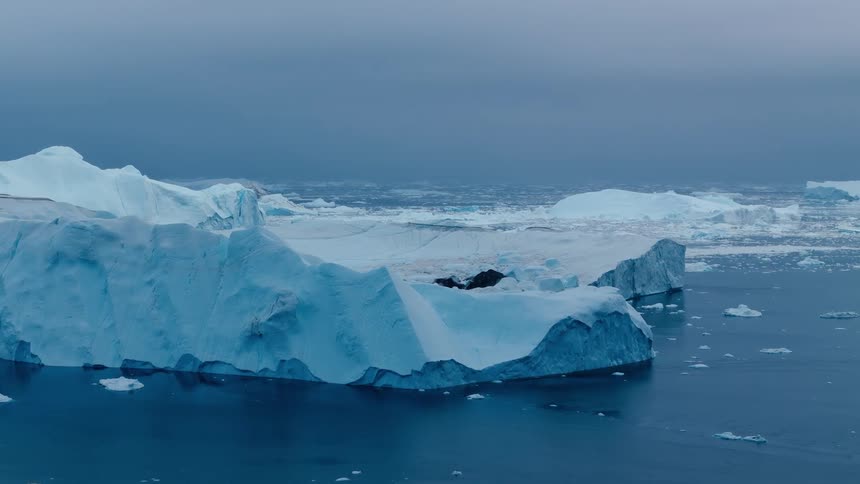 A chunky iceberg drifts on a calm gray sea with distant floes under a muted sky