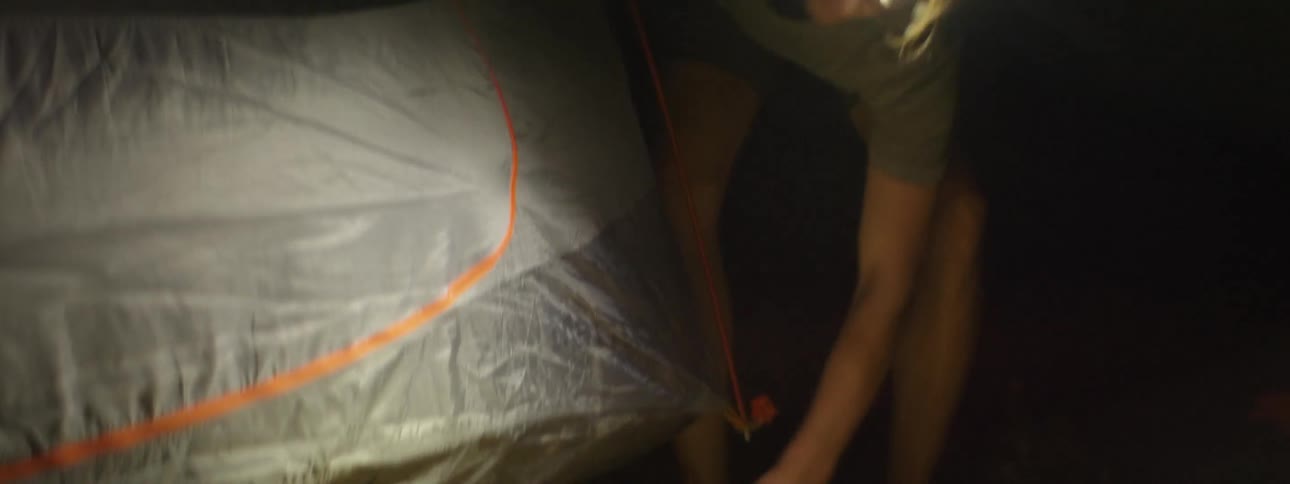 A man is putting stakes in the grass to set up a tent at night