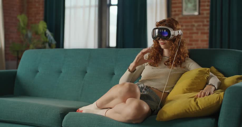 Teenage girl sits on the couch and puts on a virtual reality headset