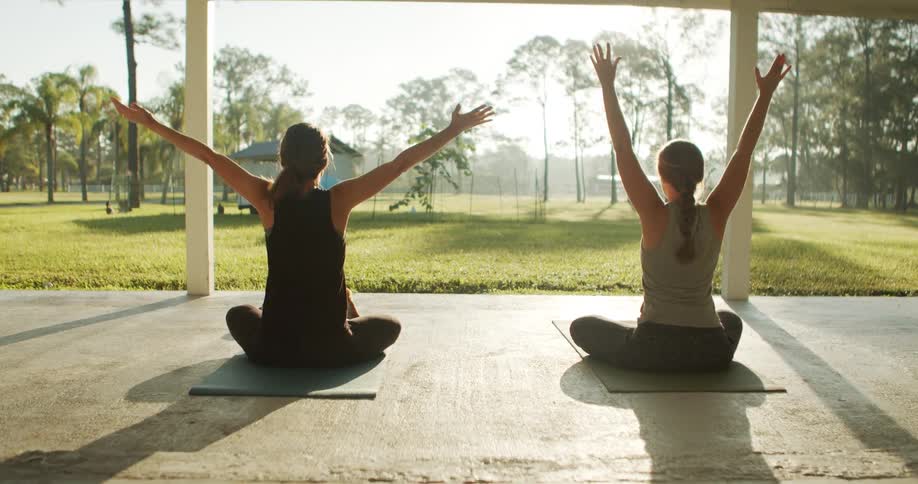 Two women practice yoga under a pavilion with grassy background