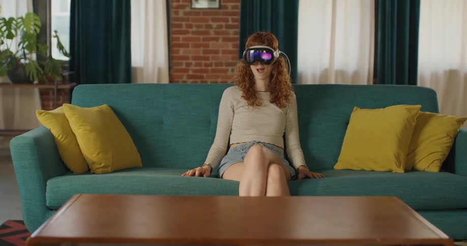 Woman wearing a vr headset sits on a couch in a living room