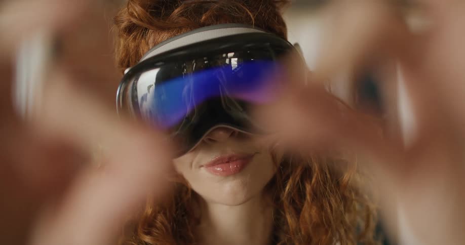 The video is a closeup shot of a woman with red curly hair wearing a sleek darkgoggled vrmr headset her face is partially obscured by her hands which are moving away from the headset to reveal her concentrating expression