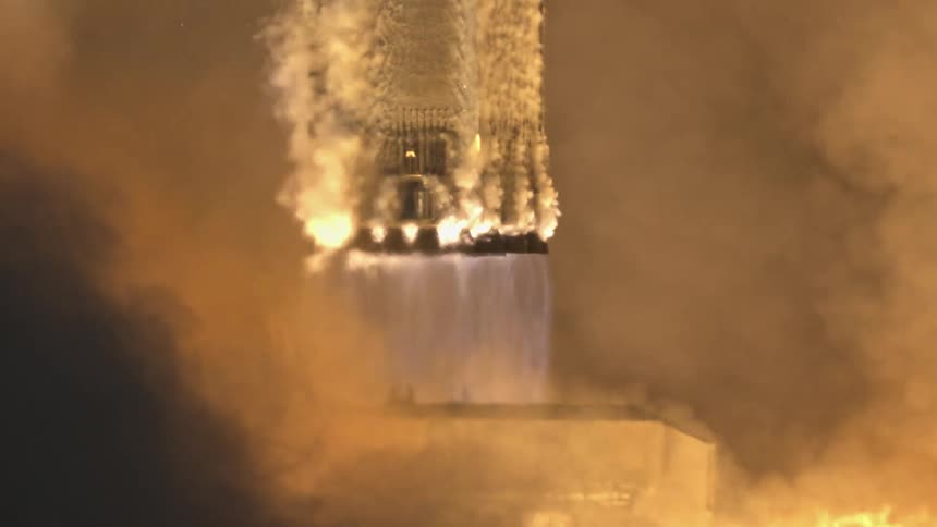 The video is an extreme closeup of the bottom of a massive rocket launch capturing the fiery blast as it ascends from the launch padthe powerful orange and yellow flames are surrounded by an immense amount of billowing dark smoke and vapor