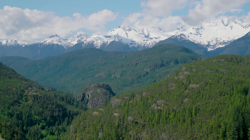 Aerial view of a forested mountain with snow covered mountains in the distance