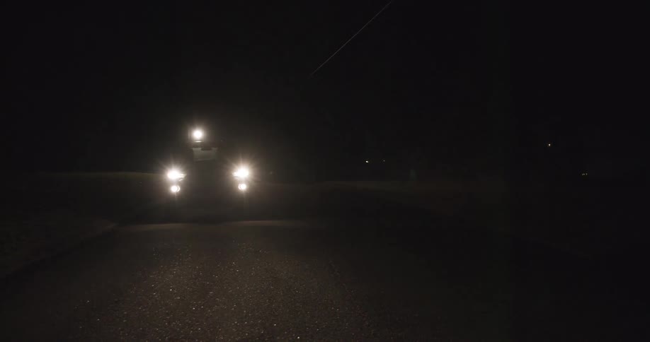 The video begins with a view of a dark road at night illuminated only by a single street light and the approaching headlights of a vehiclethe vehicle drives past the camera and its red tail lights illuminate a suburban house and garage doo
