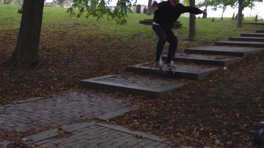A person skateboarding down stairs covered with autumn leaves in a park